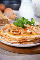Homemade thin crepe (pancakes) with honey stacked in a stack, on a table with milk and eggs in a basket. Country style food. Traditional Slavonian, pagan holiday Maslenitsa