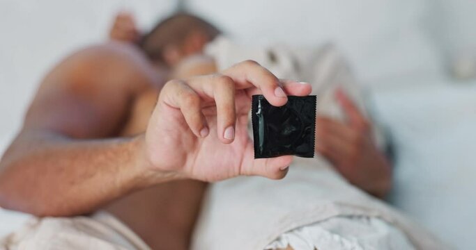 Hand, condom and people in bed for protection, sex and contraception with lust and desire on Valentines day. Intimacy, health and safety for couple bonding in bedroom with rubber and sexual moment