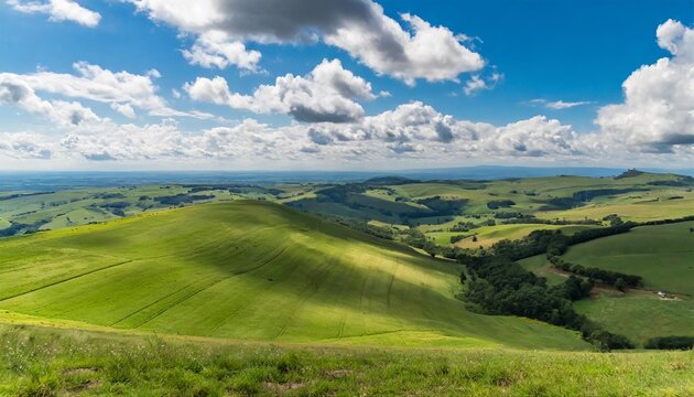 green field with rolling hills under a blue sky dotted with white clouds viewed from a high vantage point