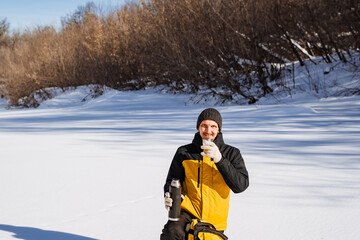 Fototapeta na wymiar a man in a yellow jacket is drinking from a thermos in the snow