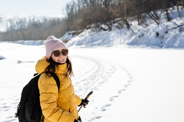 Fototapeta na wymiar Young woman in glasses and winter clothes standing on the background of snow in the forest, portrait of cute girl in winter outfit, outdoor recreation, warm jacket