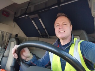 Truck Driver driving with high Visibility Vest and Red Seat Belt on, behind the Steering Wheel of a Semi Truck. interior Image. 