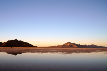 Sunset at Bonneville Salt Flats with beautiful water reflections in the salt lake and mountain silhouette in the background and blue sky near Wendover in Utah, United States