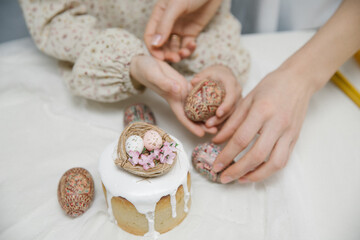 Easter cake with white glaze with a decorative bird's nest with eggs and flowers. Wooden hand painted Easter eggs in hands.