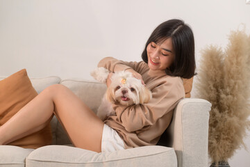 Happy young asian woman cuddling and spending time with cute dog in living room.