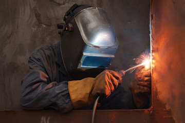 Dark tone style Welder in welding mask repairs metal wall