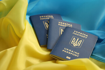 Three Ukrainian biometrical passports on folded waving flag of Ukraine country close up