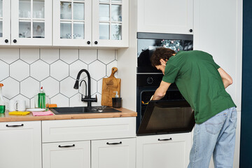 attractive man in everyday cozy attire with gloves using rag to wash oven during spring cleaning