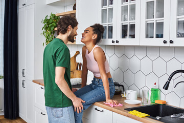 handsome man spending time with his beautiful african american girlfriend sitting on kitchen counter