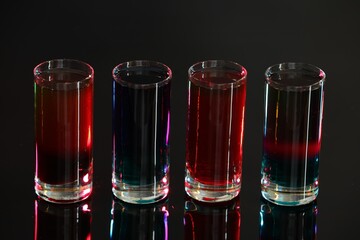 Different shooters in shot glasses on mirror surface against blurred background, closeup Alcohol...