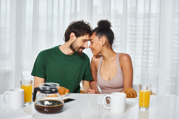 Obraz na płótnie Canvas joyous good looking multicultural couple posing lovingly together during their breakfast at home