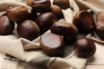 Sweet fresh edible chestnuts on light wooden table, closeup