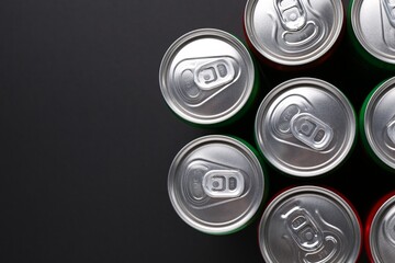 Energy drink in cans on black background, top view. Space for text