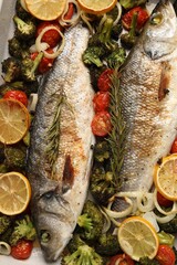 Delicious fish with vegetables and lemon in baking dish, flat lay