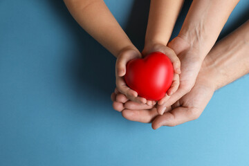 Fototapeta premium Father and his child holding red decorative heart on light blue background, top view. Space for text