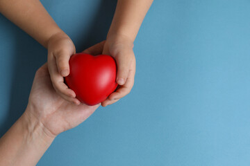 Mother and her child holding red decorative heart on light blue background, top view. Space for text