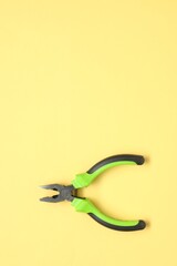 Combination pliers on yellow background, top view. Space for text