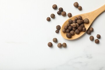 Dry allspice berries (Jamaica pepper) and spoon on white marble table, top view. Space for text