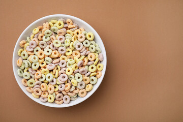 Tasty cereal rings in bowl on brown table, top view. Space for text