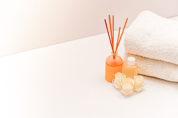 Fresh towels and reed air freshener with shower gel on light background.