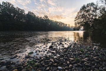 Sunrise morning at the river Mura with stones on the ground and a forest in the background