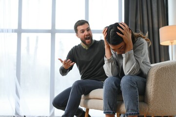 Emotional man gesturing and shouting at his wife, young couple having quarrel at home. Domestic abuse concept