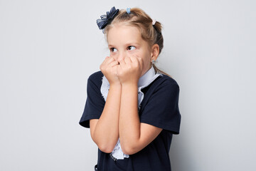 Portrait of young girl in school uniform covering mouth with hands looking away on light background