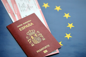 Red Spanish passport of European Union with airline tickets on blue background close up. Tourism and travel concept