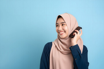 Cute young Asian girl in hijab holding a smartphone in front of a vibrant blue background