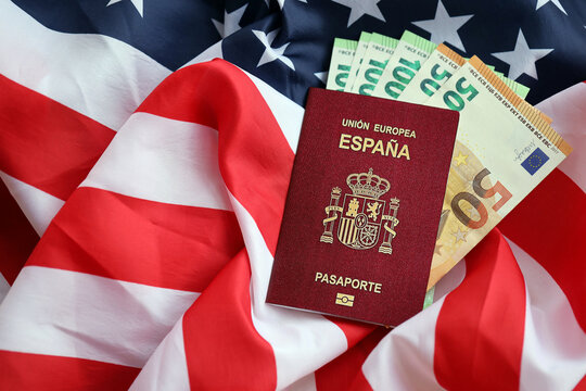 Red Spanish passport of European Union and money on United States national flag background close up. Tourism and diplomacy concept