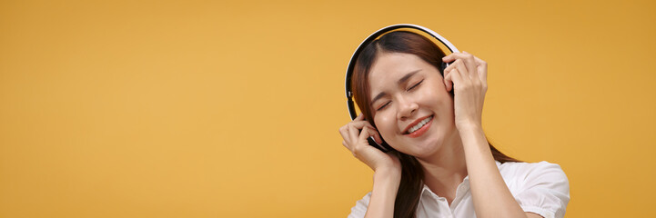 Woman wear headphone and close eyes to enjoying with listening music isolated on yellow background