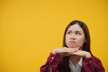 Woman putting chin on hand with unhappy face to look on advertisement isolated on yellow background