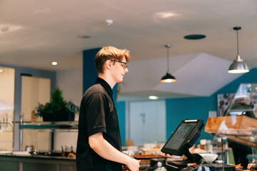 Young waiter serving customer at cash point in cafe. Man working with POS terminal. Cashier,...