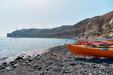 Colored kayaks lie in a row on the black sand beach (Mesa Pigadia beach). Greek Islands, Santorini, European Vacation