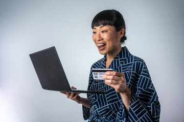 Asian woman buy online Using credit card isolated over grey background. Asian woman in kimono using laptop computer for online shopping.