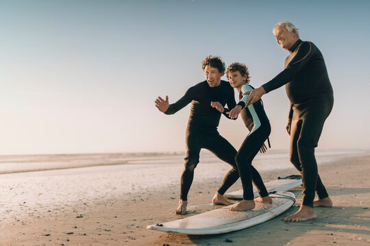 Family surf lesson on a beach at sunset with father , grandfather and son