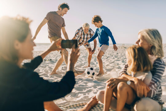 Family playing soccer on a sunny beach with kids and grandparents