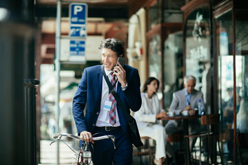 Businessman having phone call in city while going to work with bike