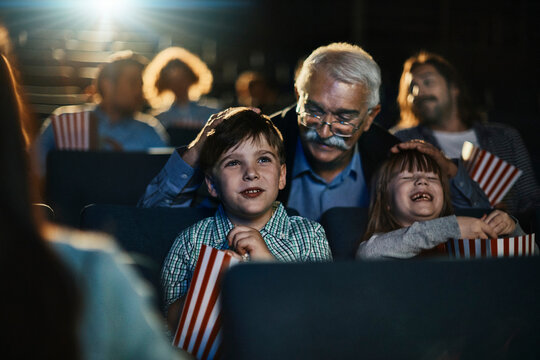 Happy grandfather watching a movie with grandchildren at cinema