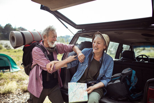 Senior couple laughing and reading a map by the car during a road trip in nature