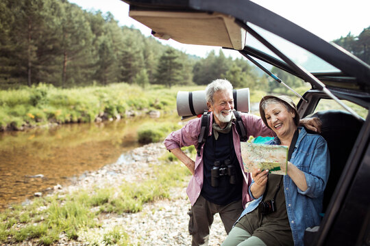 Senior couple laughing and reading a map by the car during a road trip in nature