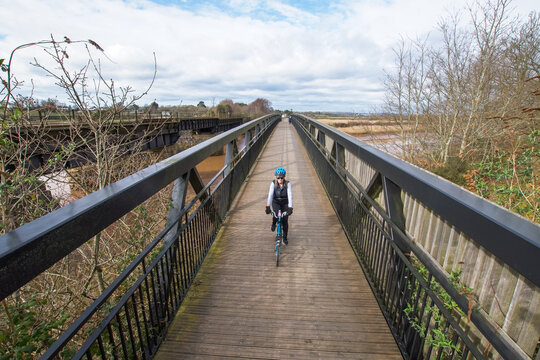 Cycling image of a lady on a bicycle riding across a bridge towards camera. Wide angle image with good symmetry. Selective focus on the cyclist. Concept image of  a healthy lifestyle and exercise. 