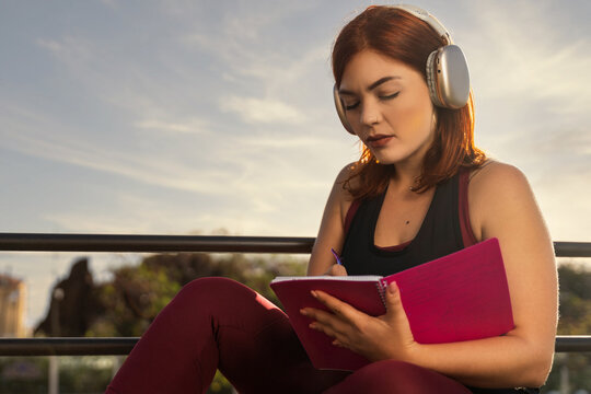 Focused Woman Writing in Journal with Headphones