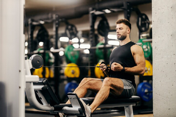 A strong muscular sportsman is working out on a pull weight machine in a gym.