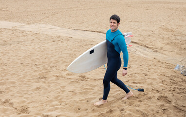 Young surfer walking on the beach with surfboard, copy space.