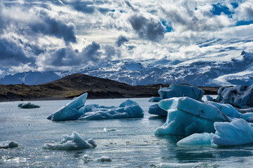 an iceberg with a mountain in the background and clouds above it