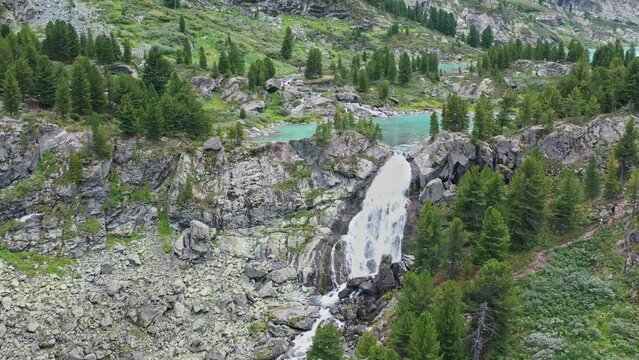 Flying over the waterfall and turquoise lake among the forest and mountains to the glacier. Altay.
