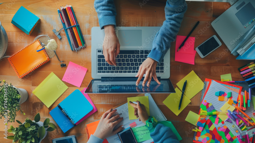 Poster top view of a workspace with hands typing on a laptop keyboard, surrounded by colorful stationery