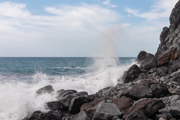 Scenic view of idyllic volcanic black stone beach Praia Garajai, Canico, Madeira island, Portugal, Europe. Sea waves smashing at shoreline of majestic Atlantic Ocean. Dramatic sky. Coastal landscape