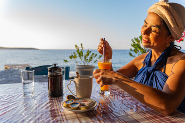 Beautiful woman on vacation in Greece enjoying a sunrise breakfast by the sea south of the Greek...